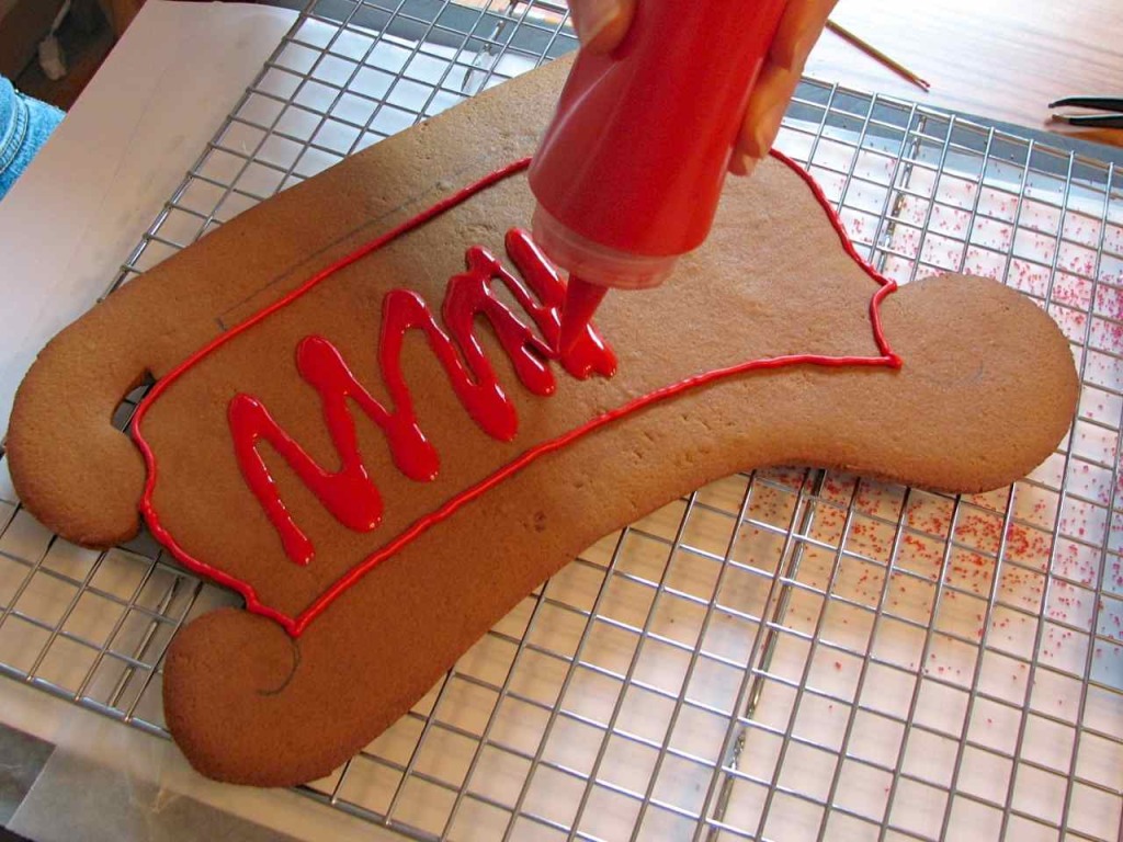 The baked side of a gingerbread sleigh getting iced - there is a piped icing border and it is being filled with "flood" icing. 
