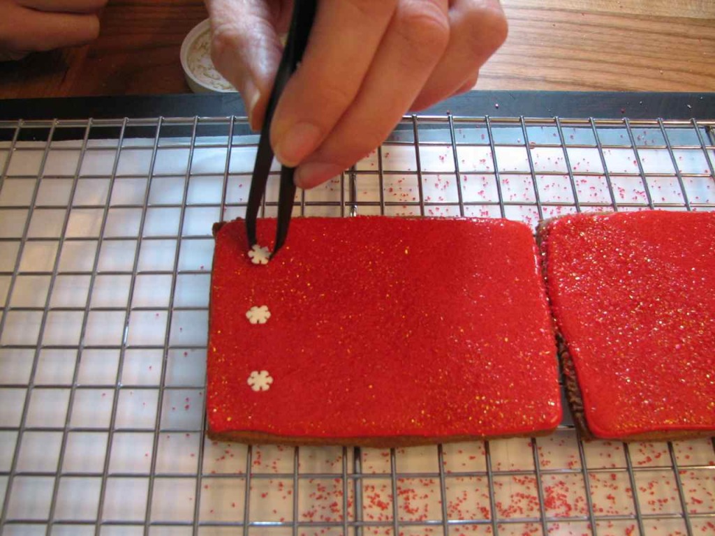 Sugar snowflakes being added with a tweezer to the still-wet, flooded and sugared box panels. 