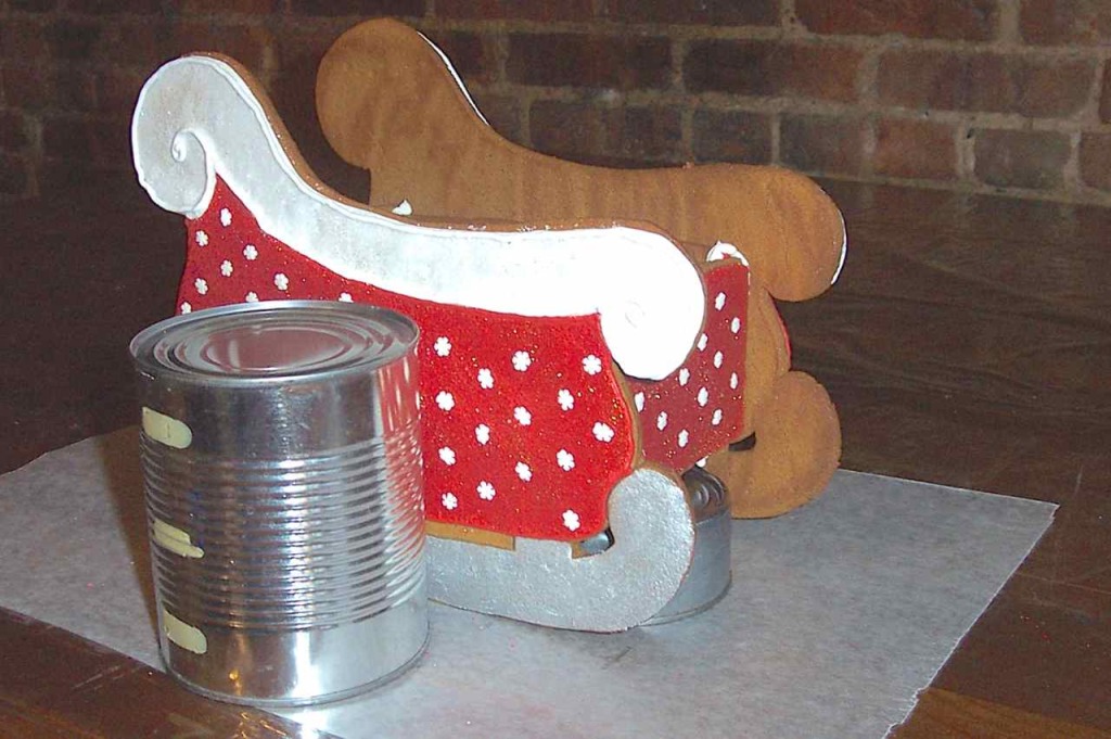 Side view of cans holding up cookie sleigh pieces while it dries.