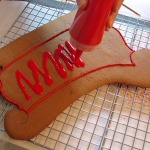 The baked side of a gingerbread sleigh getting iced - there is a piped icing border and it is being filled with "flood" icing.