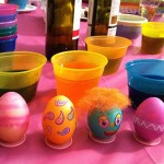 Easter egg decorating table with colored eggs, decorating supplies and wine.