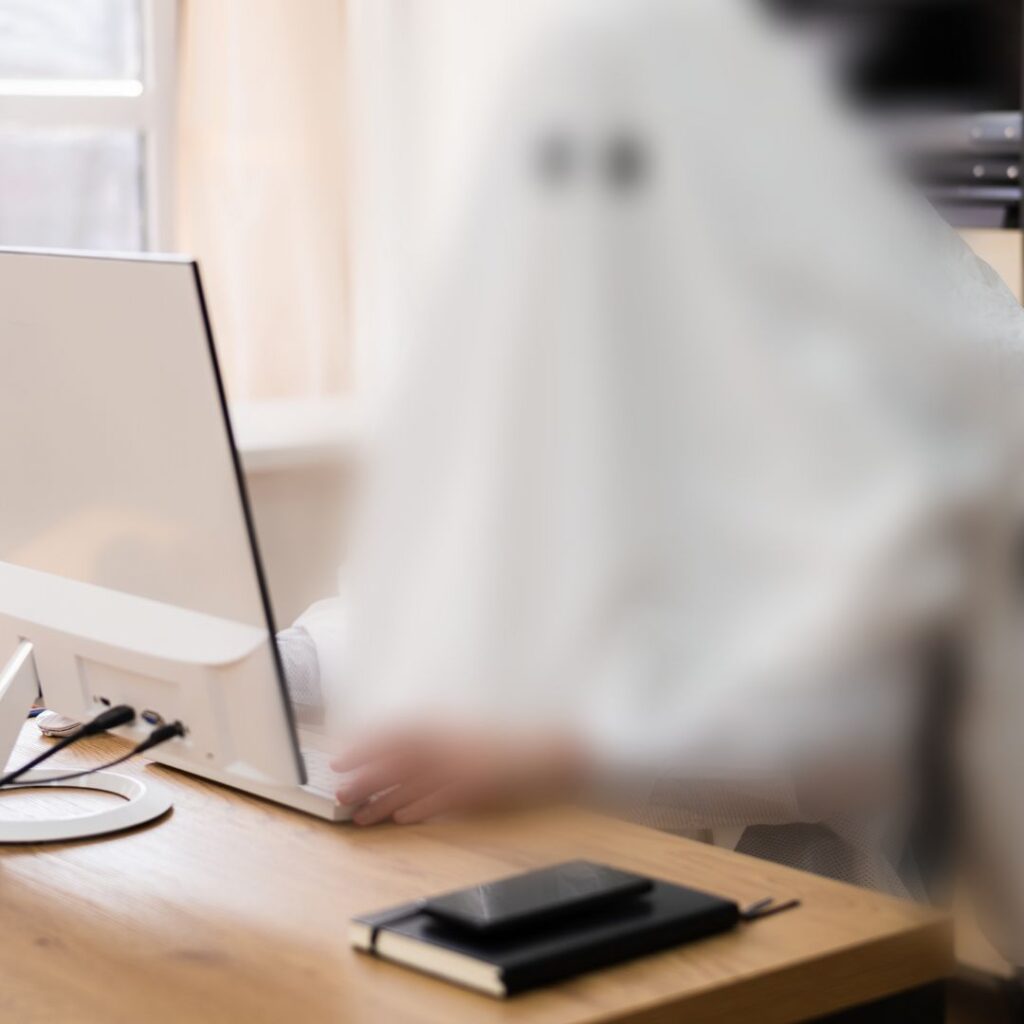 ghost - aka person in a white sheet - sitting at a laptop computer.